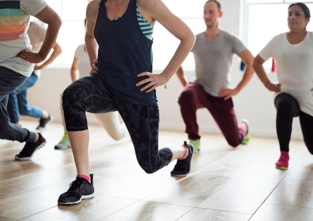 Fitness en groupe : Exercices de fentes pour tous Groupe de personnes diversifiées en tenue de sport effectuant des fentes avant lors d'un cours de fitness en salle lumineuse.